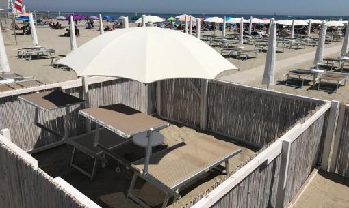 Spiaggia con ombrelloni e lettini, area riservata con recinzione.