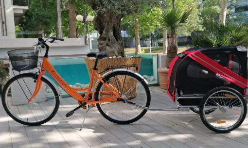 Bicicletta arancione con rimorchio per animali, parcheggiata all'aperto.