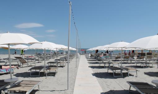 Spiaggia soleggiata con ombrelloni bianchi e sdraio, atmosfera rilassante e serena.