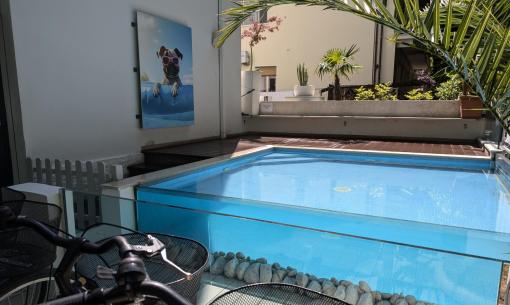 Piscina luminosa con bici, palme e un cane dipinto con occhiali da sole.