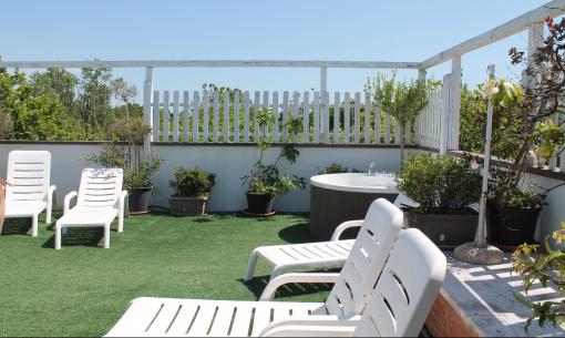Terrazza soleggiata con sdraio bianche e vasca idromassaggio, circondata da verde rigoglioso.