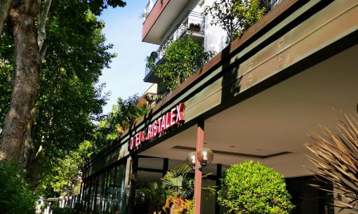Edificio moderno con giardino e insegna luminosa su strada alberata.